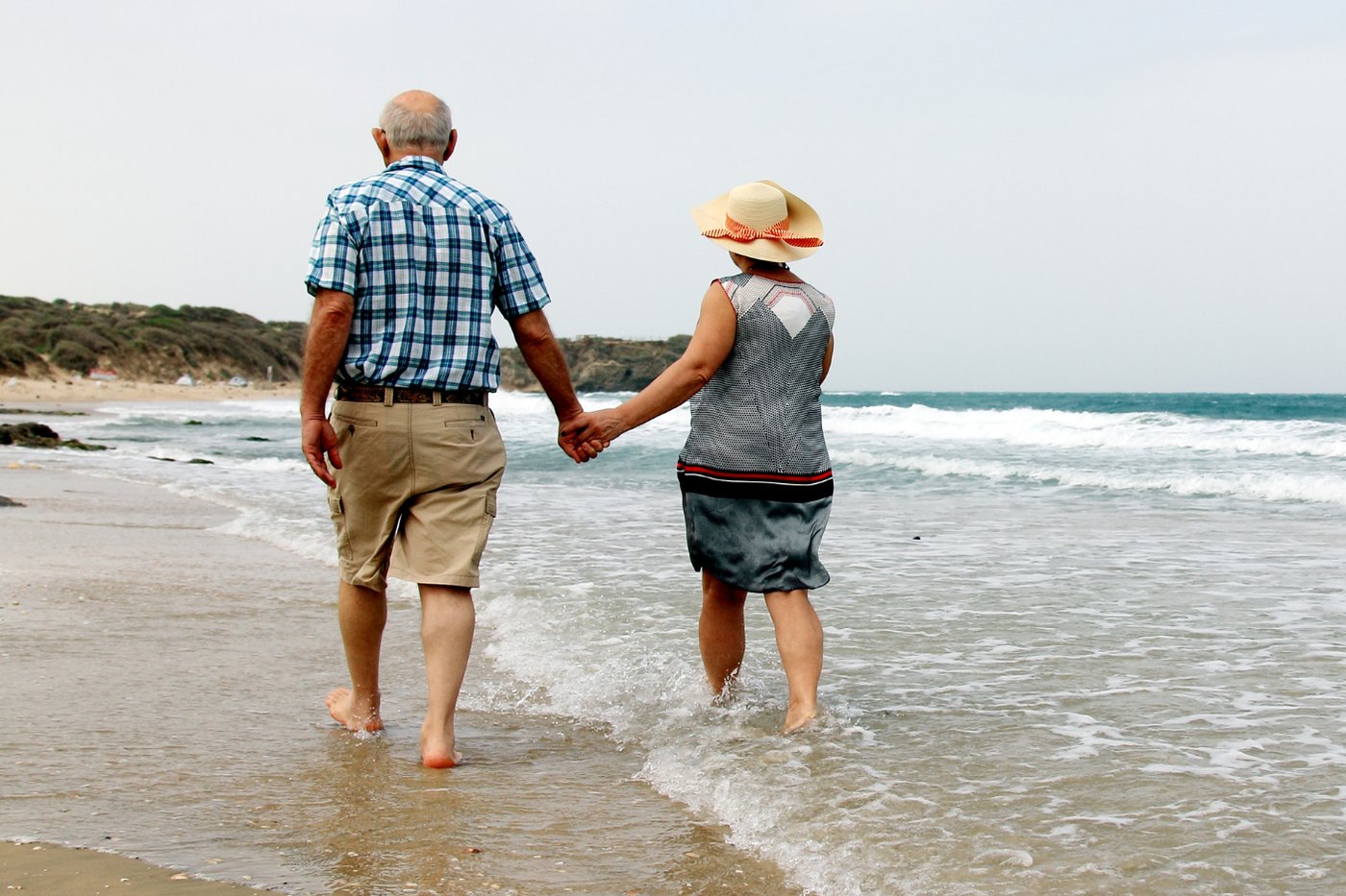 An older couple walking hand in hand along the water's edge at a beach
